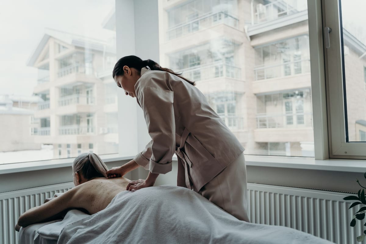 A massage therapist working on a draped patient's back