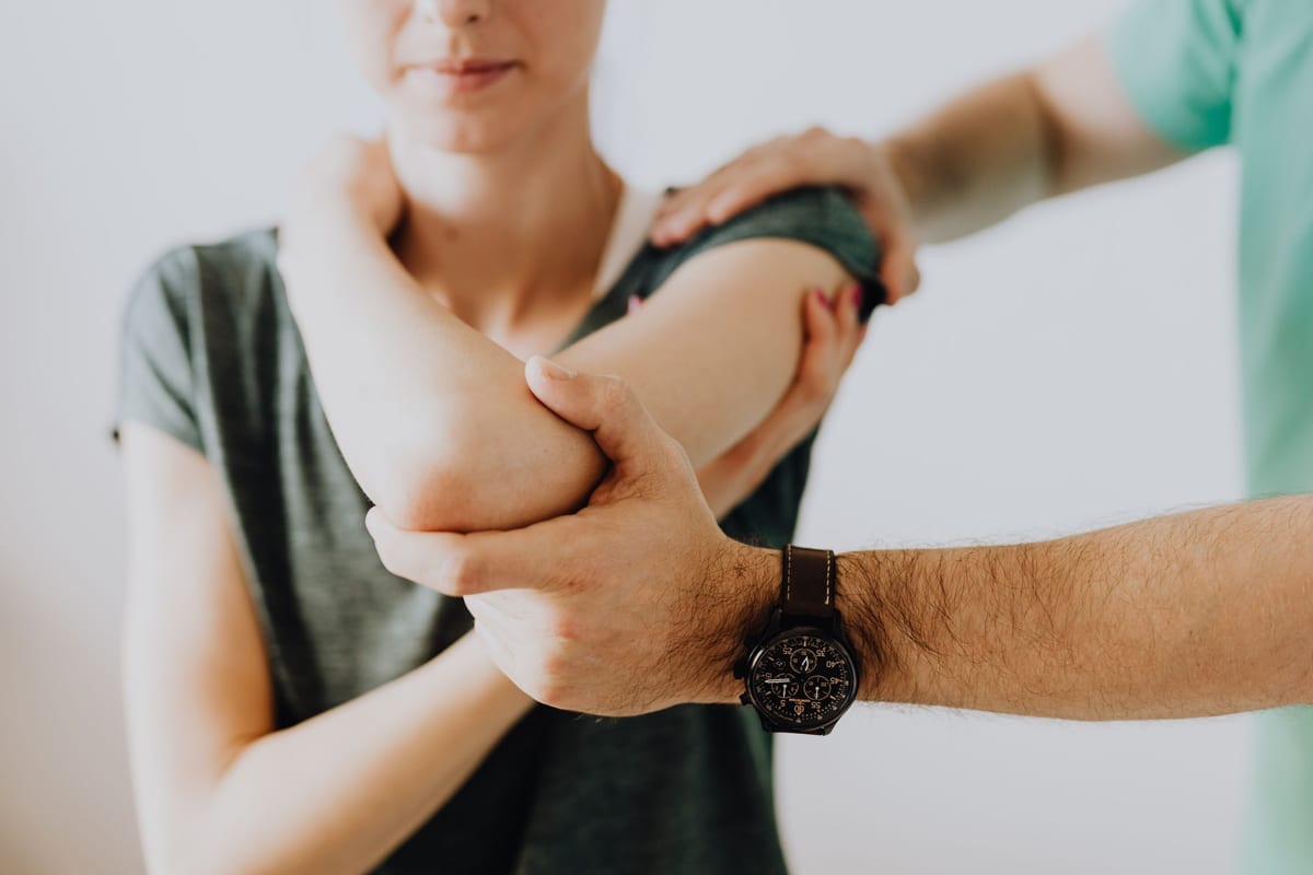 A clinician supporting a patient's arm and shoulder during an assessment