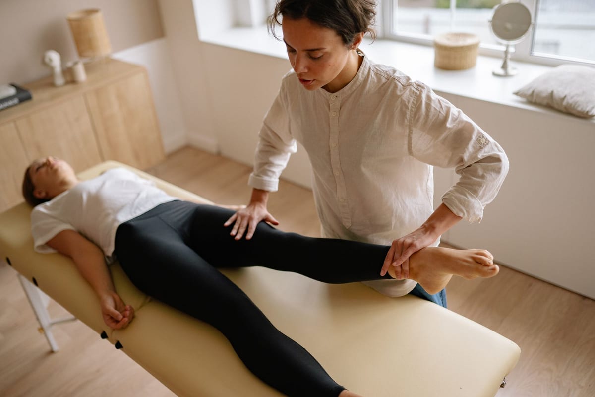 A clinician assessing a patient's raised leg on a treatment table